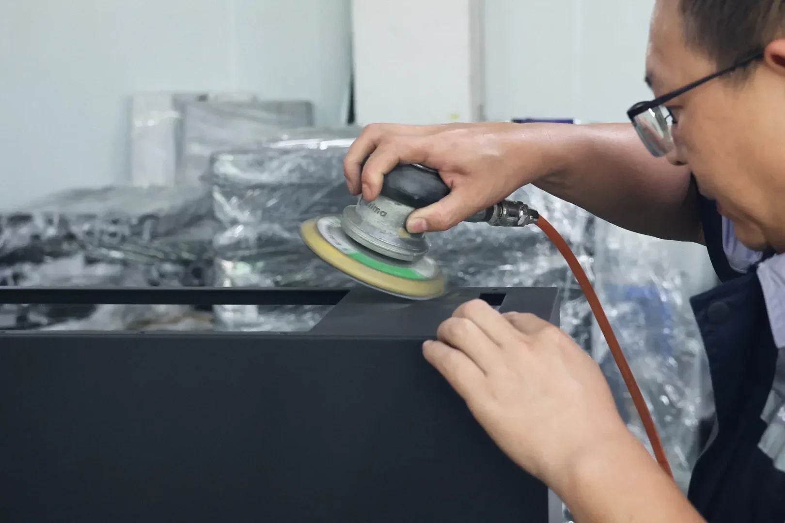 Worker sanding metal cabinet surface with pneumatic orbital sander for smooth finishing