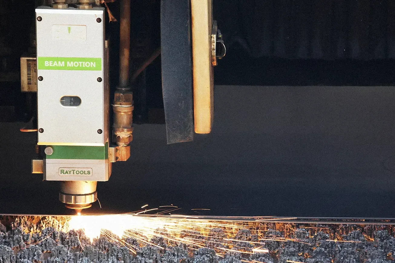 Fiber laser cutting head precisely cutting flat metal sheet with flying sparks in manufacturing workshop