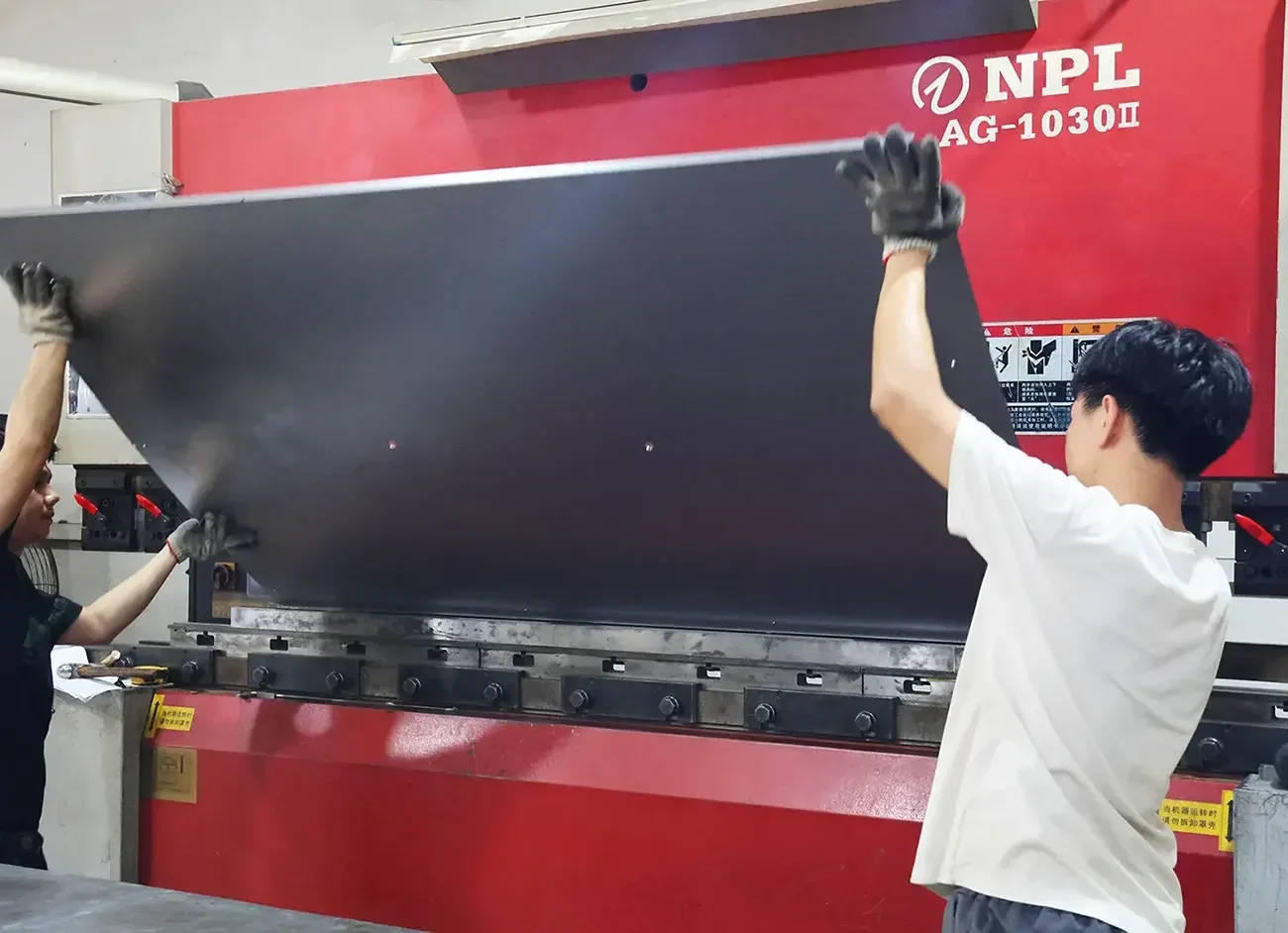 Workers feeding metal sheet into CNC press brake for precision sheet metal bending