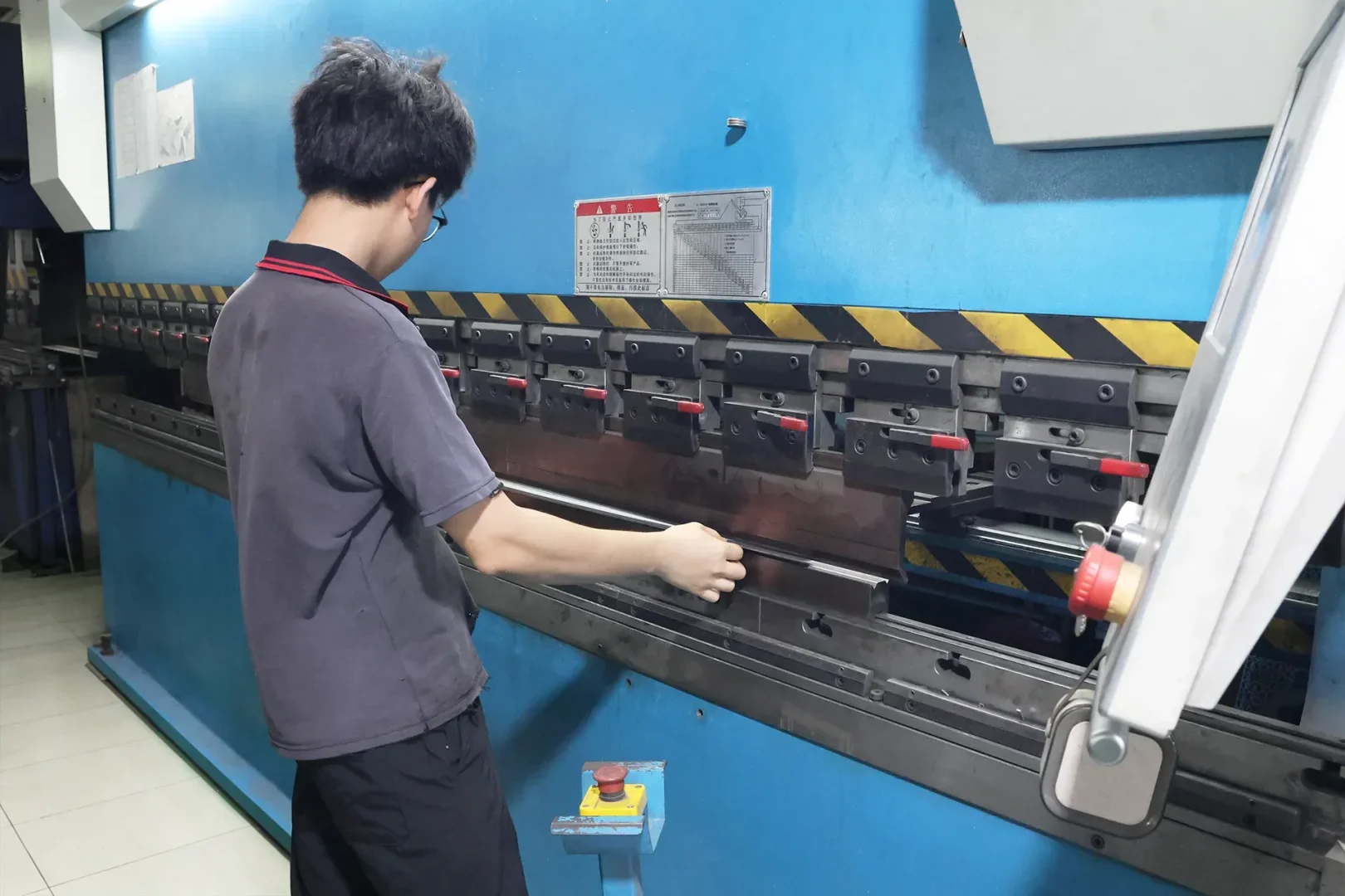 Worker operating CNC press brake to accurately bend metal sheets in manufacturing workshop