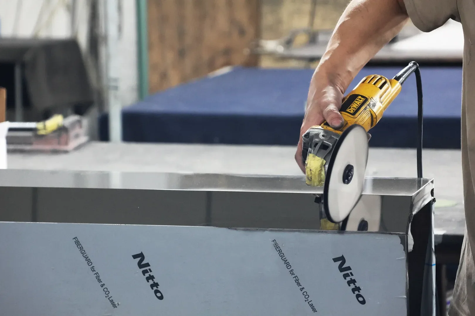 Worker polishing stainless steel panel with angle grinder to create uniform brushed finish for custom electrical enclosures