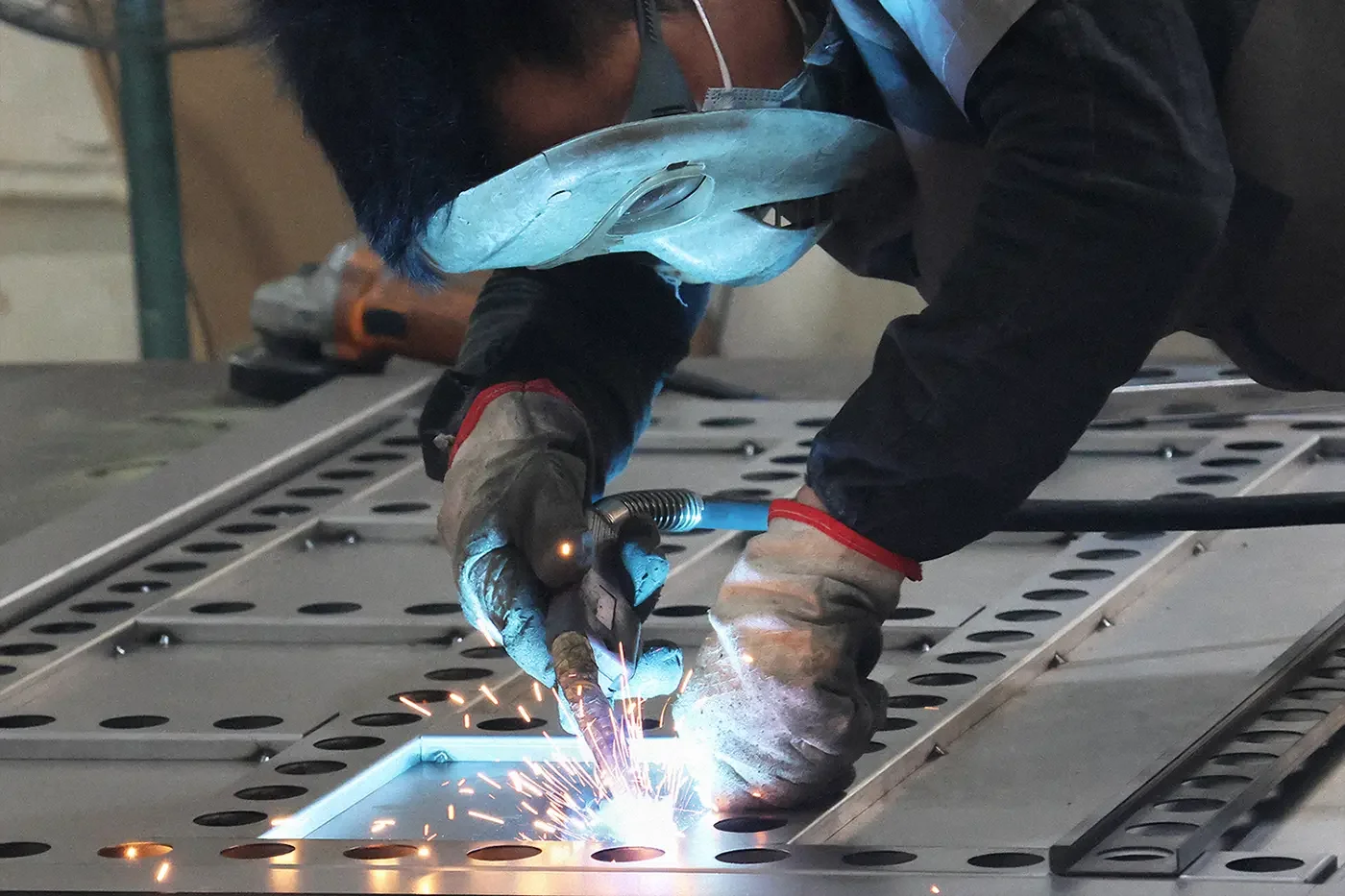 Factory welder performing MIG welding on sheet metal cabinet parts in fabrication workshop